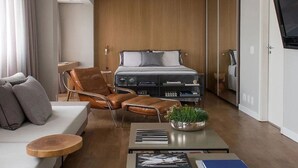 Une chambre d’hôtel moderne équipée d’un lit, d’un canapé, d’un fauteuil, d’une table basse et d’un téléviseur.