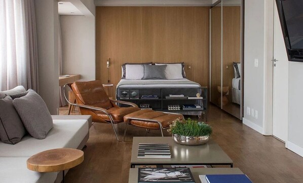 Une chambre d’hôtel moderne équipée d’un lit, d’un canapé, d’un fauteuil, d’une table basse et d’un téléviseur.
