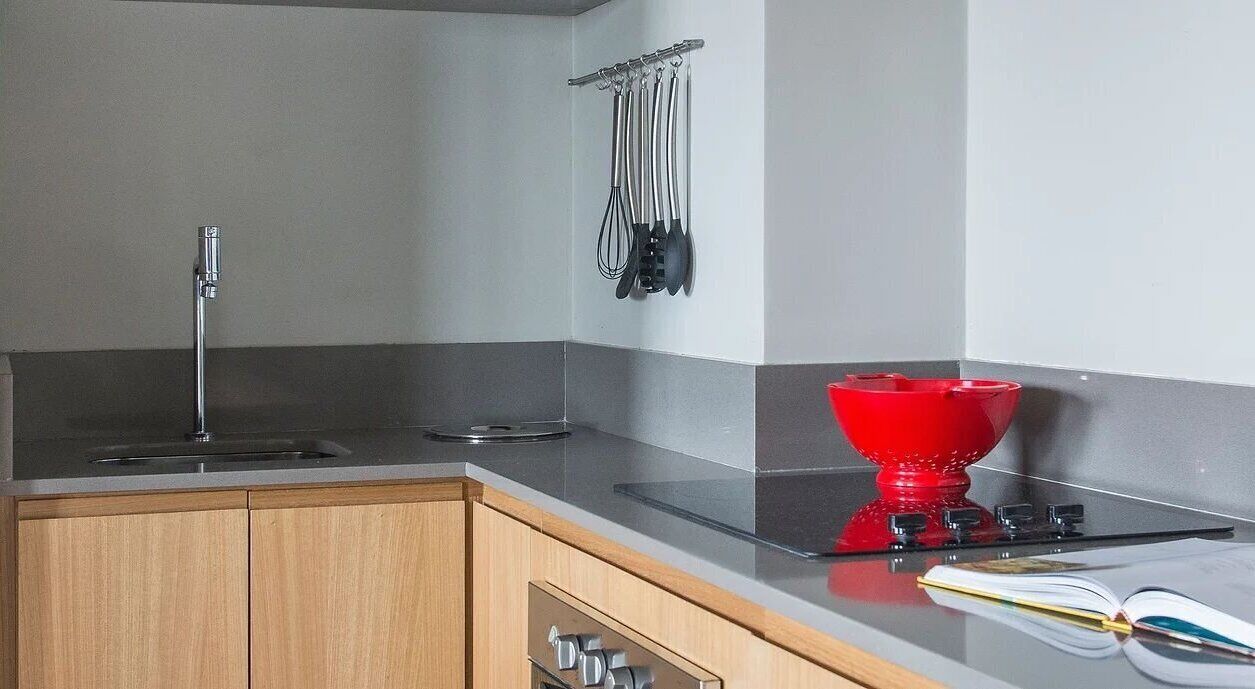 Uma cozinha com pia de aço inoxidável, chaleira vermelha e utensílios pendurados.
