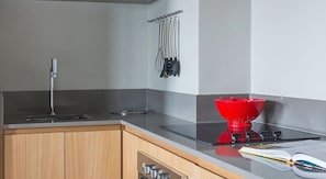 A kitchen with a stainless steel sink, a red kettle, and a set of hanging utensils.
