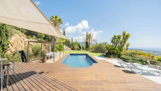 Una terraza de madera con piscina, mobiliario exterior y vistas del paisaje.