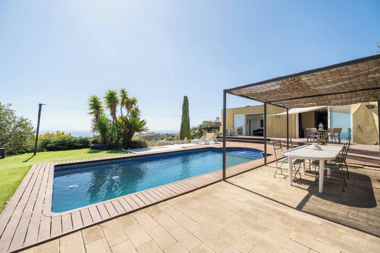 Ein Schwimmbecken mit Holzterrasse, einer überdachten Veranda und Blick auf das Meer.
