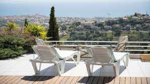 Una terraza con dos sillones blancos y vistas a un paisaje urbano costero.