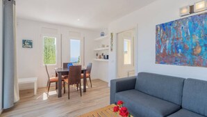 Una sala moderna con un sofá gris, una mesa de comedor de madera y sillas. Hay un cuadro en la pared y una ventana con vistas.