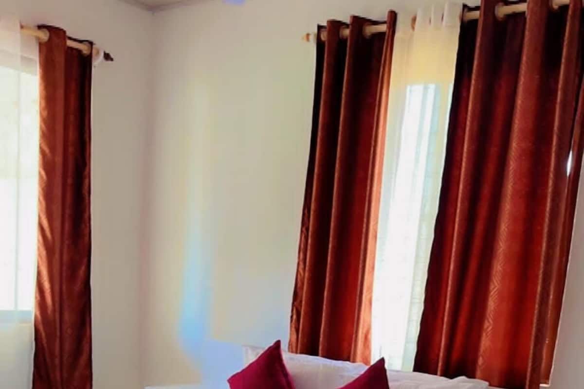 A hotel room with a bed, a nightstand, a ceiling fan, and curtains.