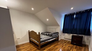 A bedroom with a wooden bed, a radiator, a window with curtains, and a wooden floor. - Lovely 6-bed House in Windsor (Windsor)