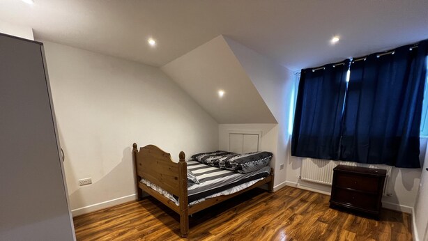 A bedroom with a wooden bed, a radiator, a window with curtains, and a wooden floor. - Lovely 6-bed House in Windsor (Windsor)