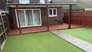 A backyard with artificial grass, a wooden deck, and a brick house. - Lovely 6-bed House in Windsor (Windsor)