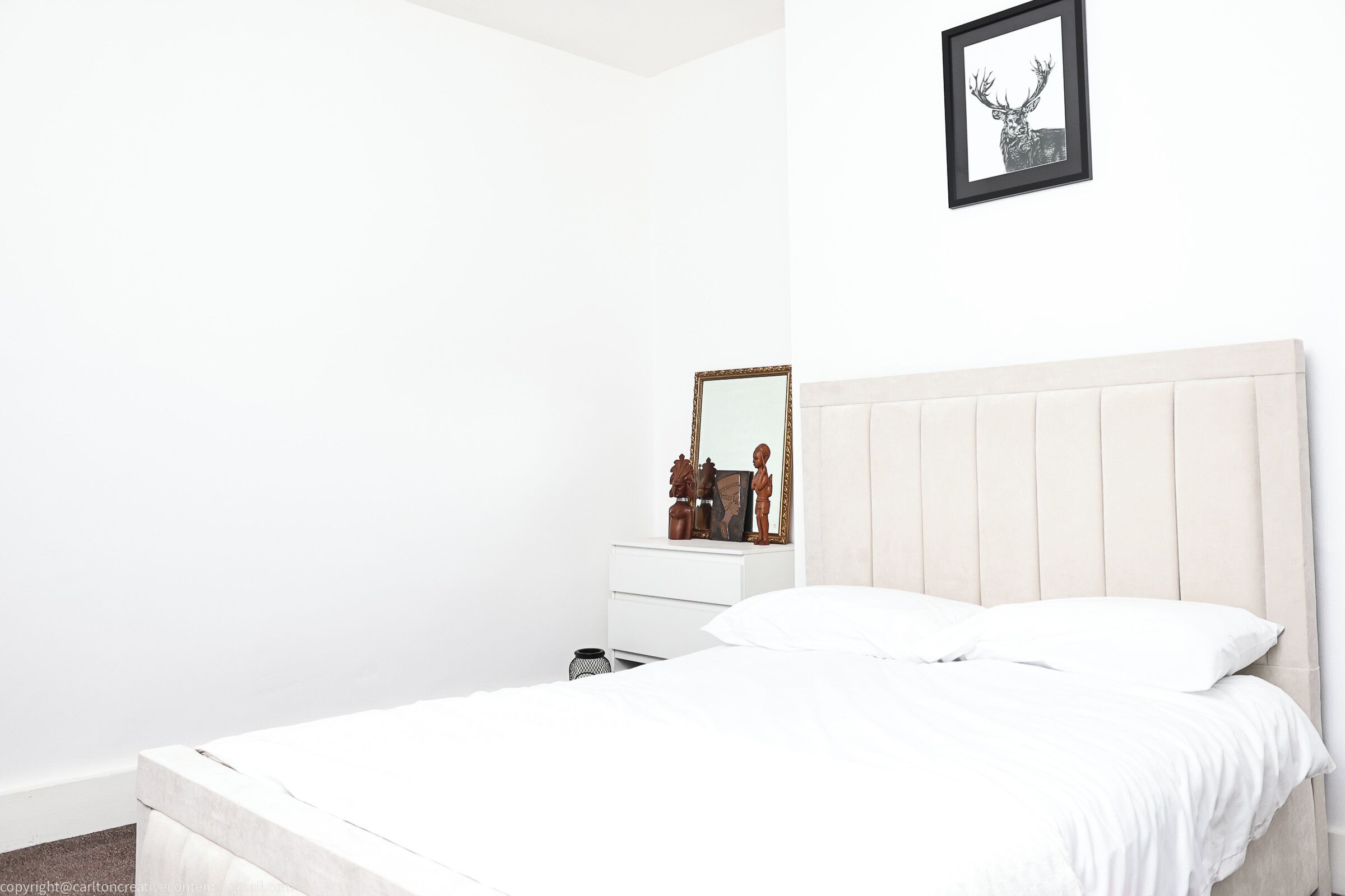 Een minimalistische slaapkamer met een bed, een dressoir en een spiegel.