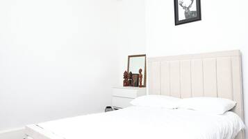 Een minimalistische slaapkamer met een bed, een dressoir en een spiegel.