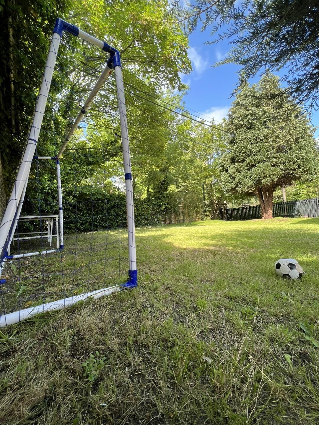 A grassy outdoor area with a metal structure, possibly a swing set, and a soccer ball on the ground.