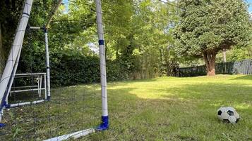 A grassy outdoor area with a metal structure, possibly a swing set, and a soccer ball on the ground.