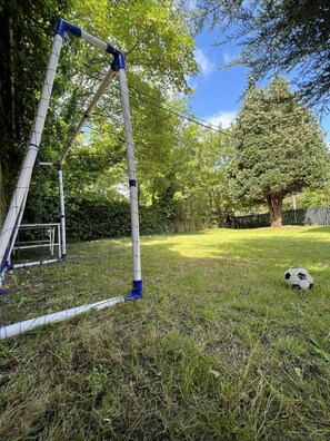 A grassy outdoor area with a metal structure, possibly a swing set, and a soccer ball on the ground. - 4-bed Cottage, Sleeps 8, Walk to Thames Garden (Hampton)