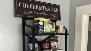 Una barra de café y té montada en la pared, con estantes que contienen varias cajas de té, un hervidor y tazas.