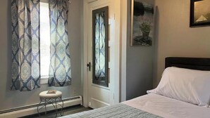 Un dormitorio con cama, un radiador, una mesita y cortinas.