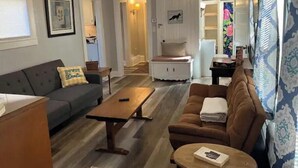 Una sala de estar con un sofá, una mesa de centro y un sofá marrón. Se ve una puerta que da a otra habitación.