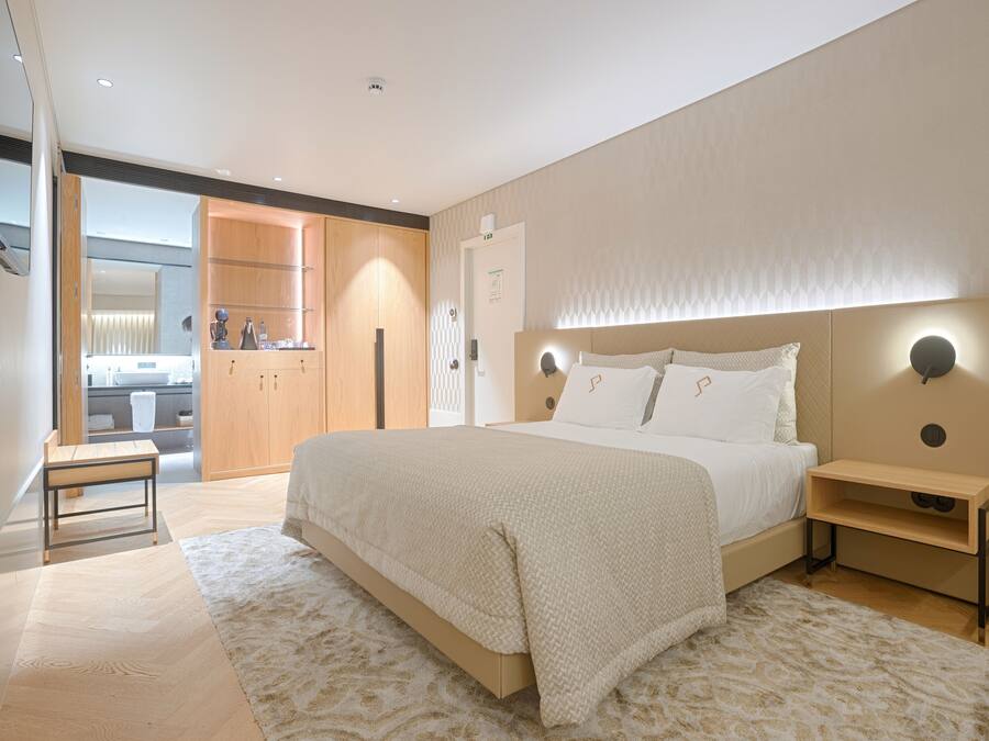 A modern bedroom with a large bed, bedside tables, a nightstand, and a view into the bathroom.