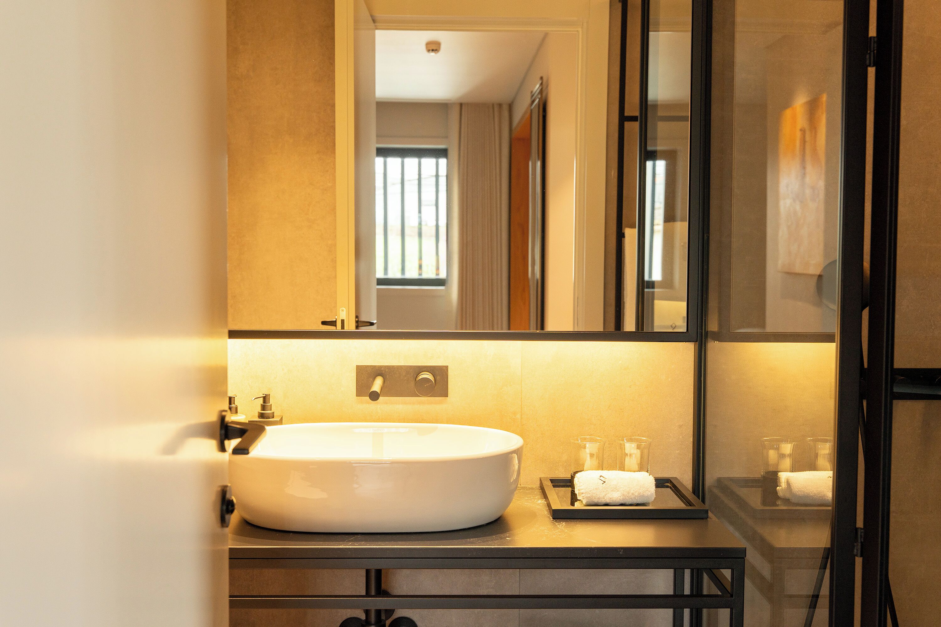 A modern bathroom with a large oval sink, a mirror, and a window.