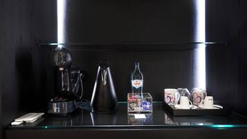 A dark room with a coffee maker, a kettle, a bottle, and a tray with cups and saucers.