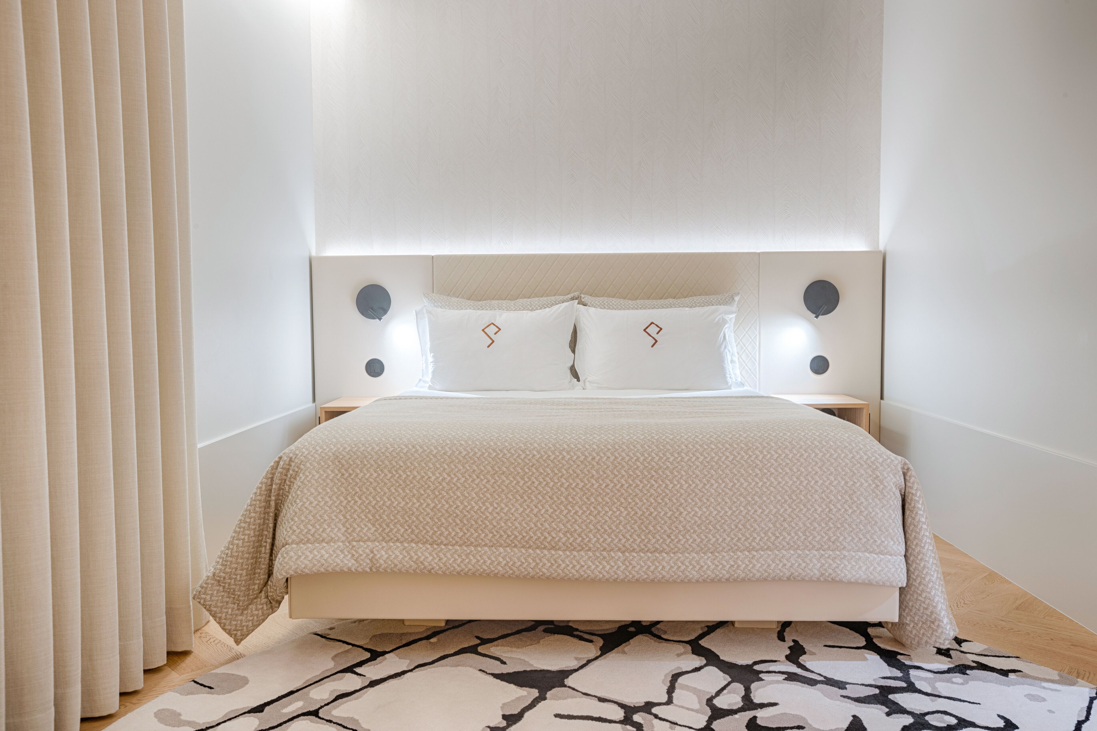 Een moderne slaapkamer met een bed, nachtkastjes en een kamerkleed met dessin.