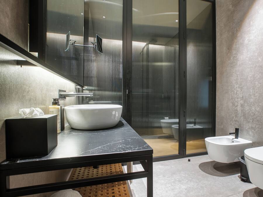 A modern bathroom with a large mirror, a white sink, a bidet, and a toilet.