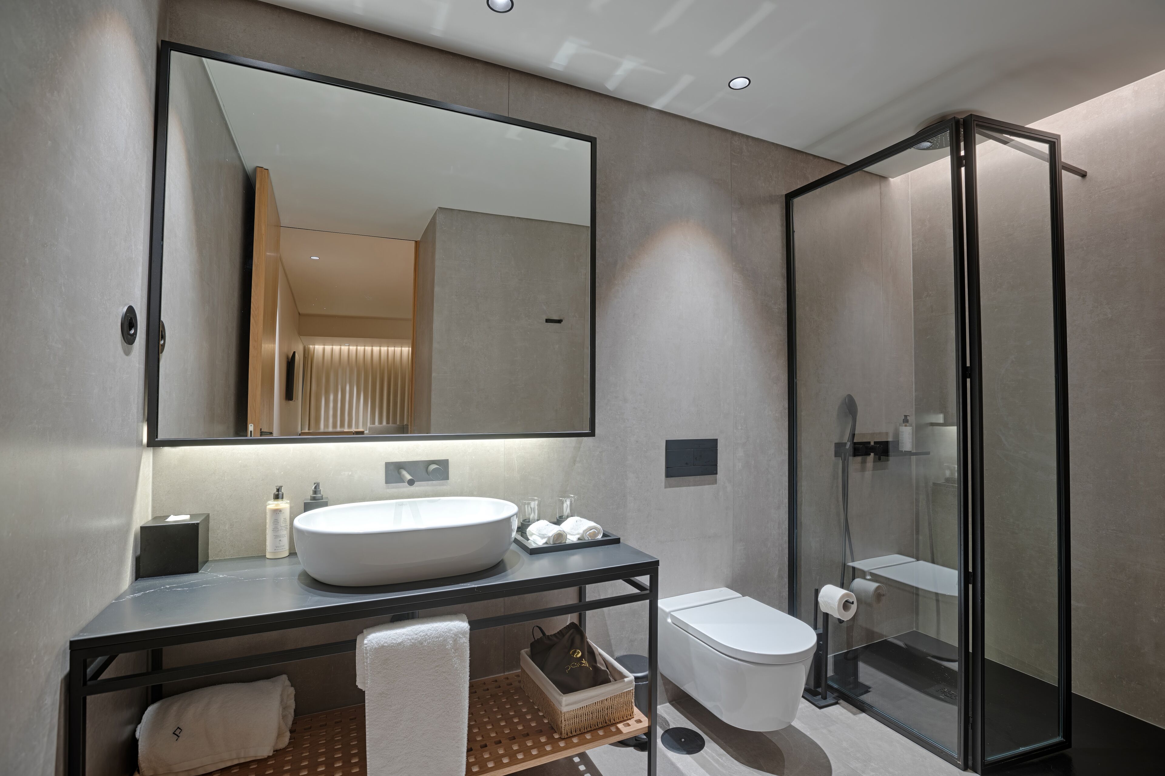 Un baño moderno con un espejo grande, un lavamanos, un inodoro y una ducha con mampara de vidrio.