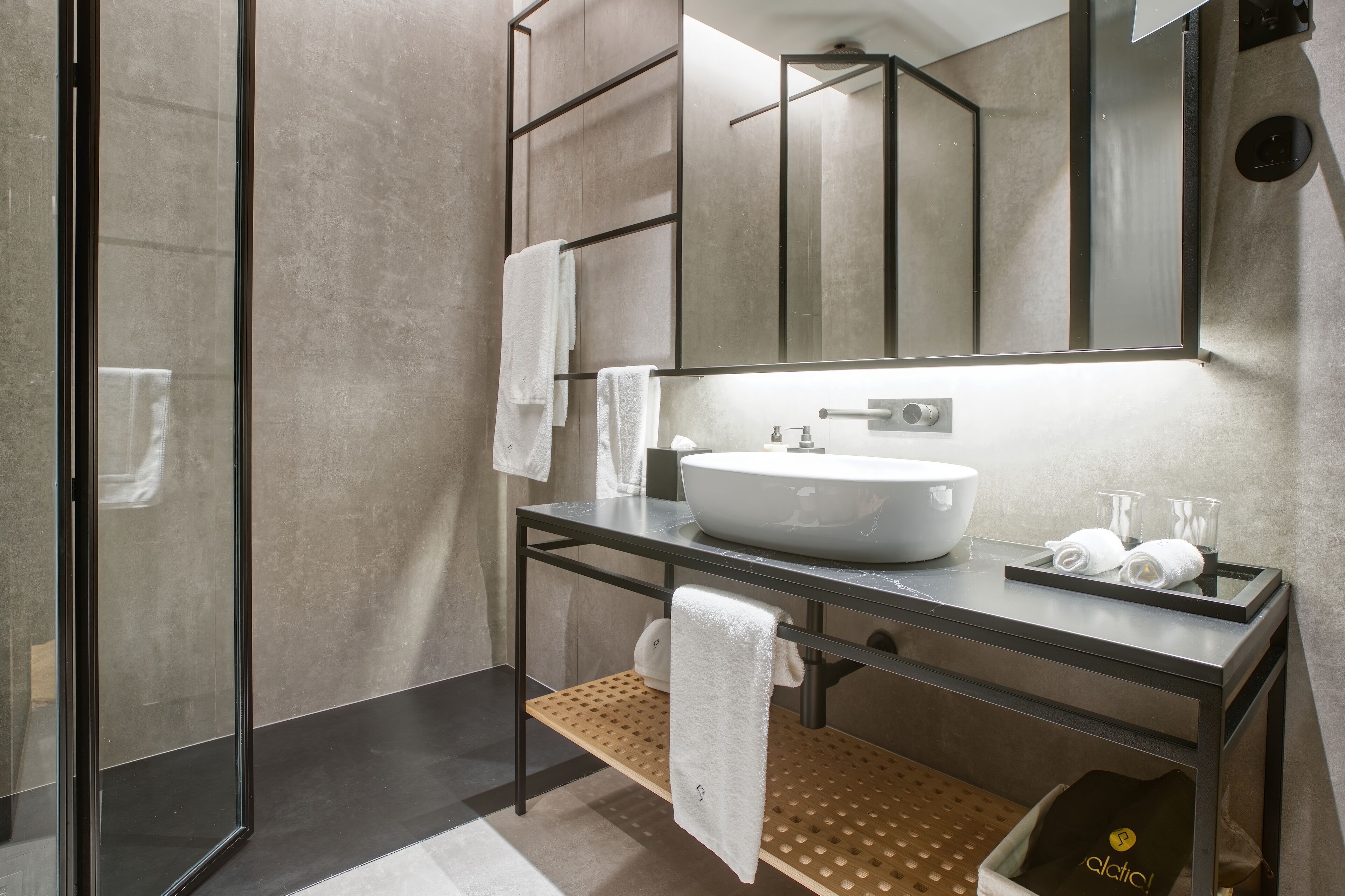 Un baño moderno con cabina de ducha de vidrio, un espejo grande, un lavabo con recipiente y un estante de madera con toallas.