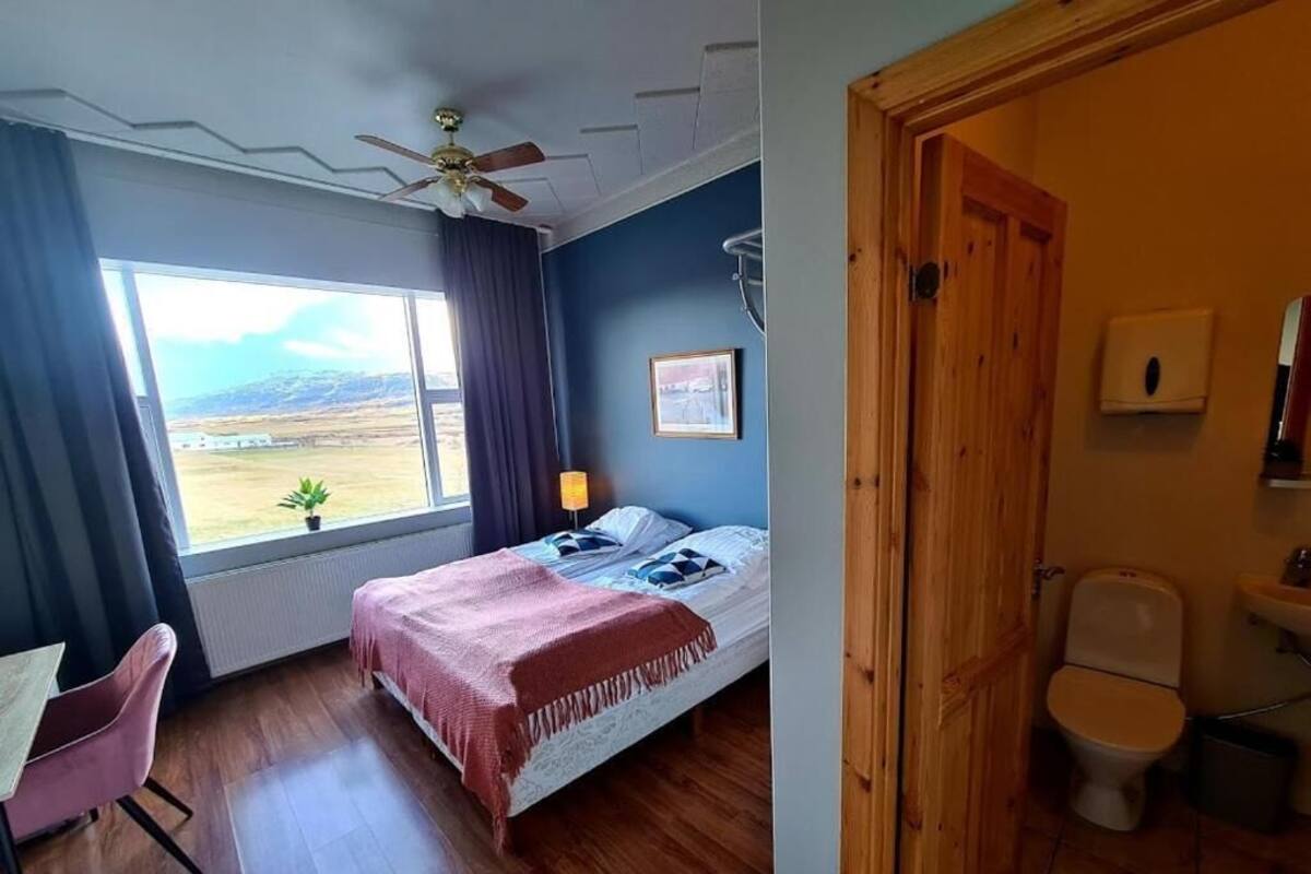 A bedroom with a bed, a chair, a window with a view, and a bathroom with a toilet and sink.