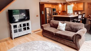 Ein modernes Wohnzimmer mit einer Couch, einem Fernseher und einem Essbereich, im Hintergrund eine Küche.