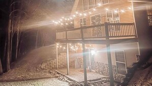 Eine Holzhütte mit Balkon, Lichterketten und einem Steinfundament.