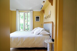 A bedroom with a bed, a bedside table, a window with curtains, a picture on the wall, and a wooden headboard. - Hôtel de la Plage (Lège-Cap-Ferret)