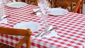 Une rangée de tables recouvertes de nappes à carreaux, avec des chaises en bois, chacune étant dressée avec des assiettes, des couverts et des verres à vin.