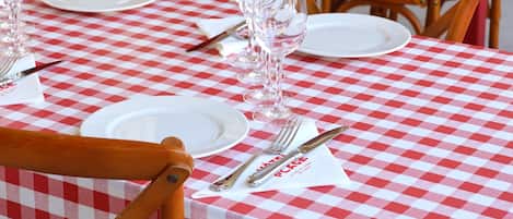 A row of tables with checkered tablecloths and wooden chairs, each set with plates, cutlery, and wine glasses.