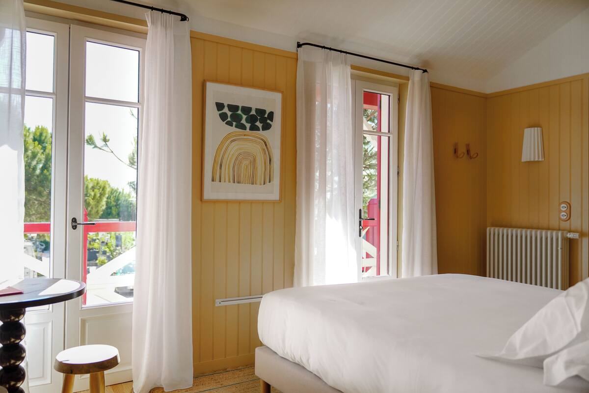 Une chambre à coucher avec un lit, une fenêtre avec des rideaux, un radiateur et une œuvre d’art encadrée accrochée au mur.