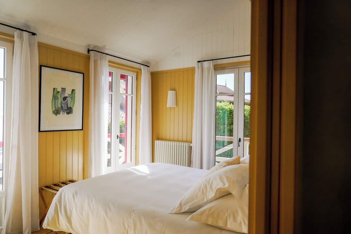 Une chambre à coucher avec un lit, une fenêtre avec des rideaux, un radiateur et un tableau encadré au mur.