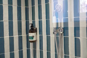 A bathroom with a blue and white striped tile wall, a bottle of shampoo, and a shower fixture. - Hôtel de la Plage (Lège-Cap-Ferret)