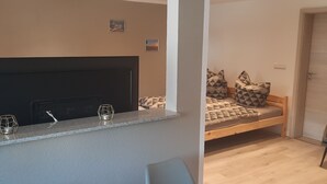 Ein modernes Zimmer mit Essbereich, einem Bett mit gemusterten Kissen und einem Fernseher auf einem schwarzen Lowboard.