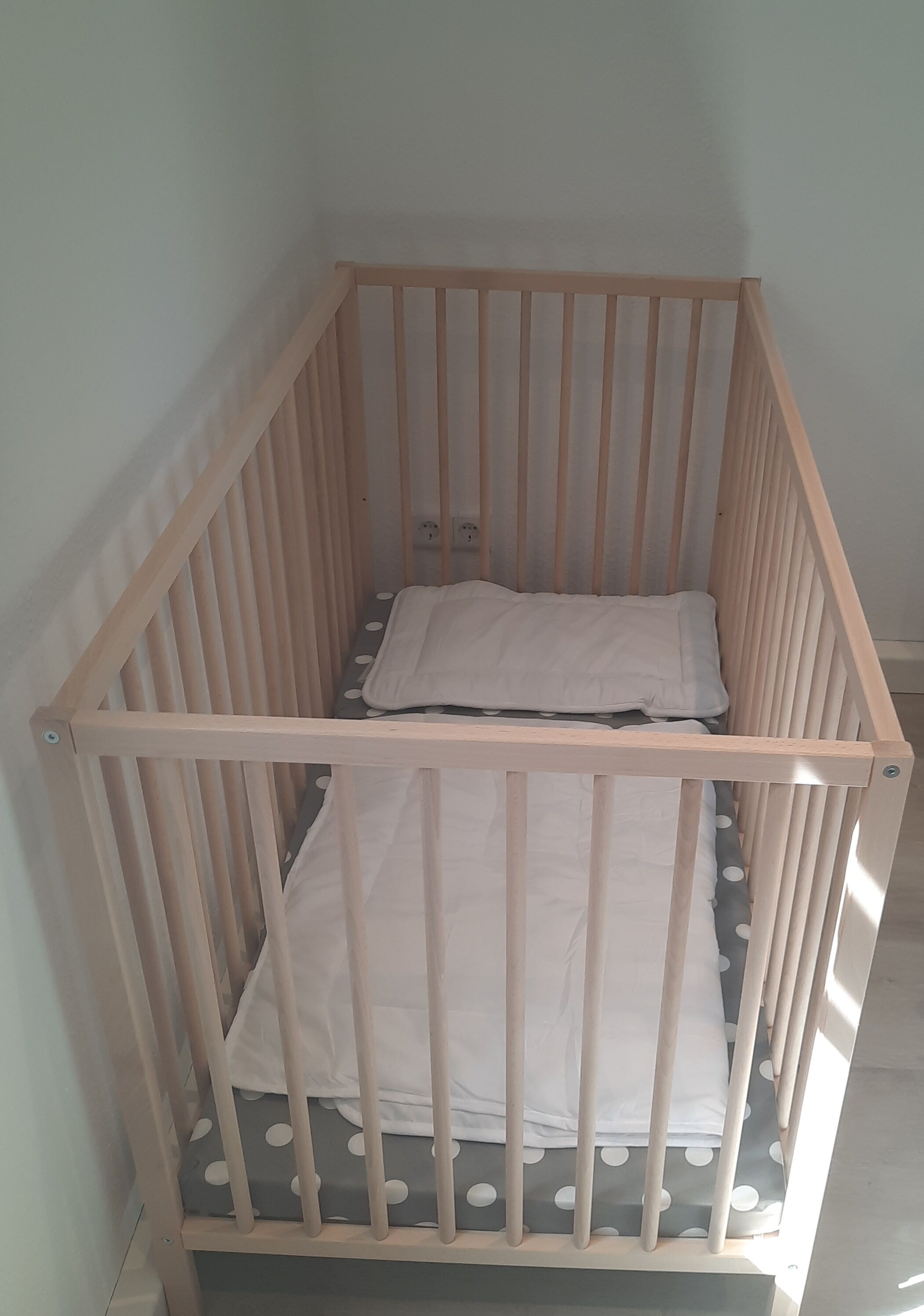 Un berceau en bois avec un matelas gris et du linge de lit blanc.