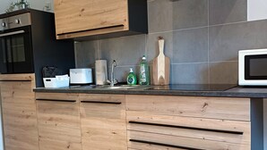 Eine moderne Küche mit Holzschränken, einem eingebauten Backofen, einer Mikrowelle und einer Edelstahl-Dunstabzugshaube.