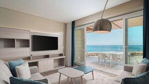 A modern living room with a flat-screen TV, a coffee table, and a sofa. There is a large window with a view of the beach and ocean. - Dom Pedro Residences  (Loulé)