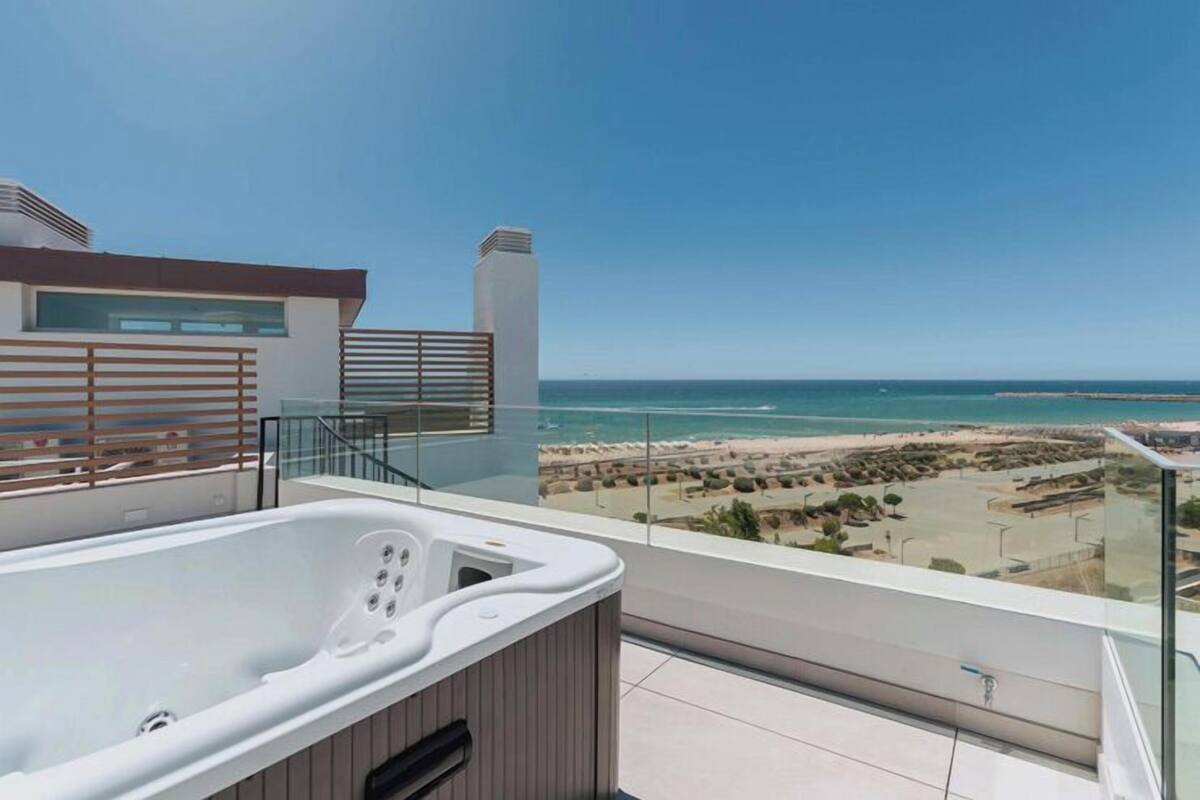A balcony with a hot tub overlooking a beach.