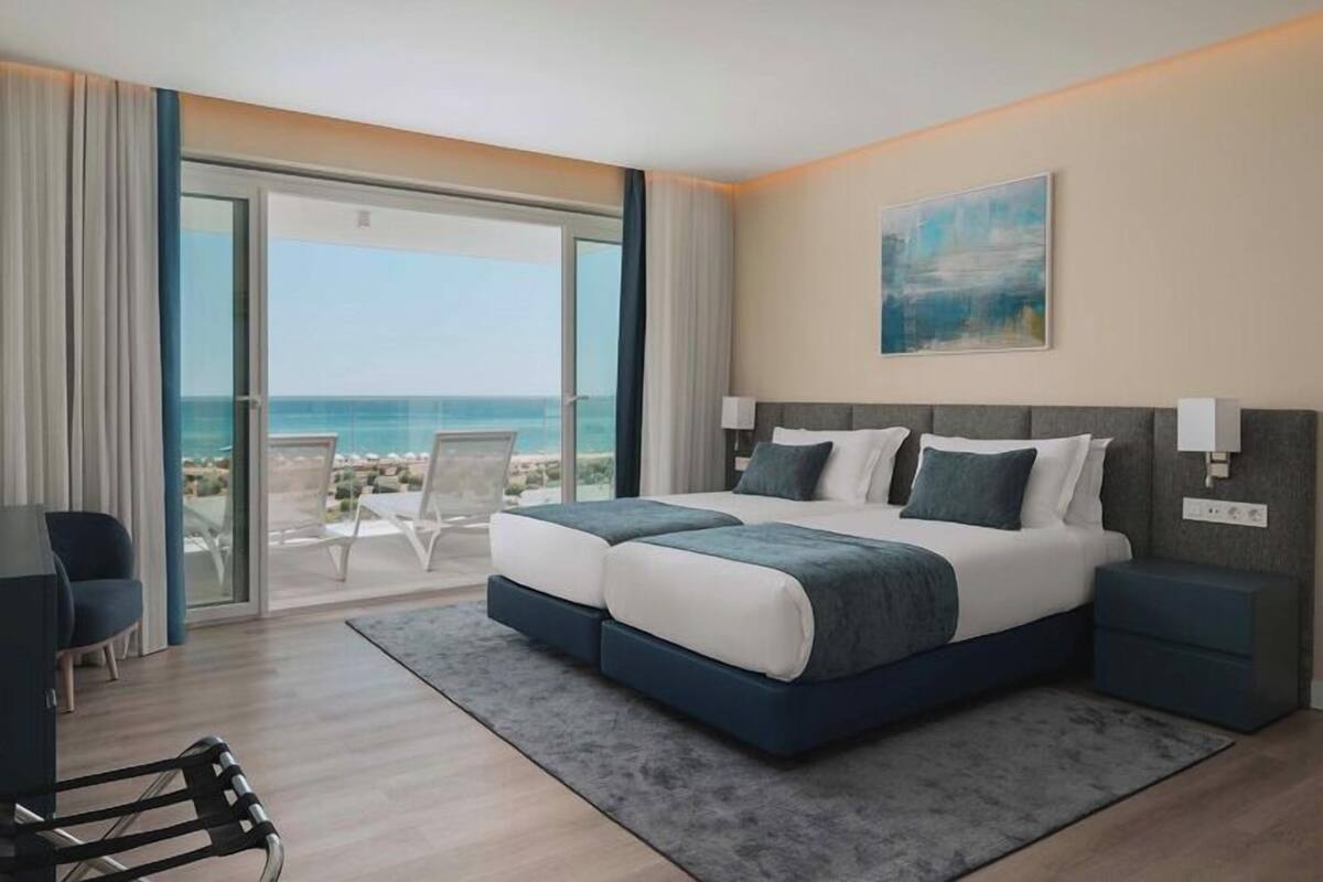 A hotel room with a large bed, a desk, and a view of the beach.