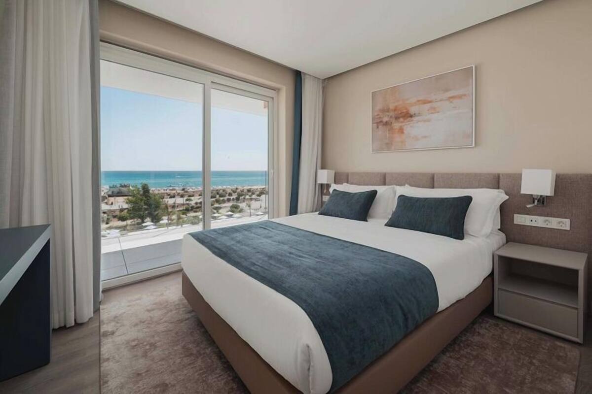 A hotel room with a large bed, a desk, and a view of the beach.