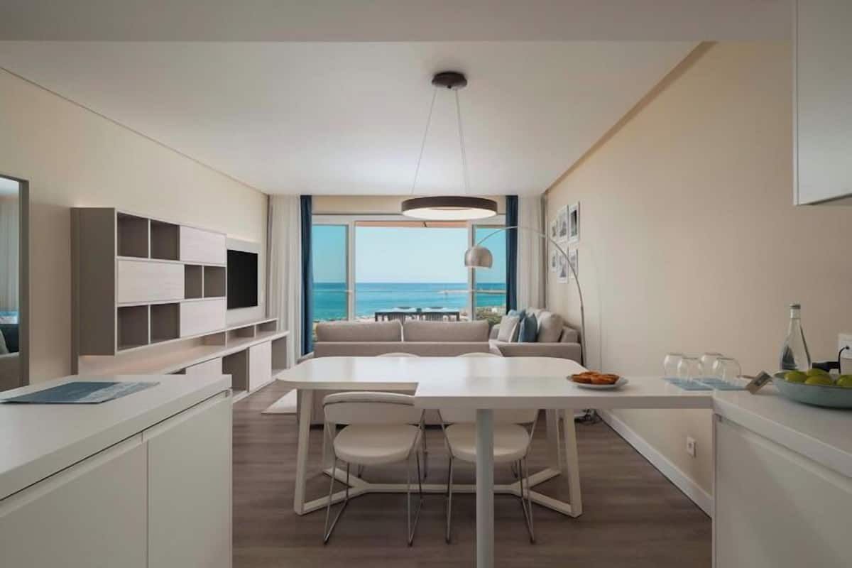 A modern kitchen with a dining area, large windows with a view of the sea, and a ceiling light fixture.