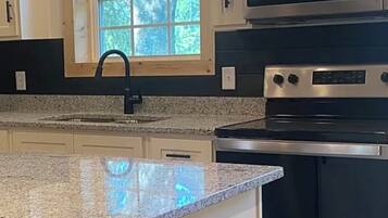 A kitchen with a granite countertop, stainless steel appliances, and a window with a view of trees.