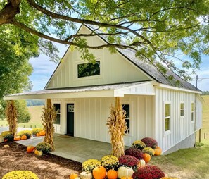 A white barn with a covered porch, surrounded by autumnal decorations and pumpkins.