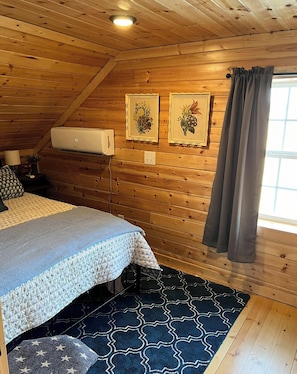 A cozy room with a bed, a wall-mounted air conditioner, and a window with curtains.
