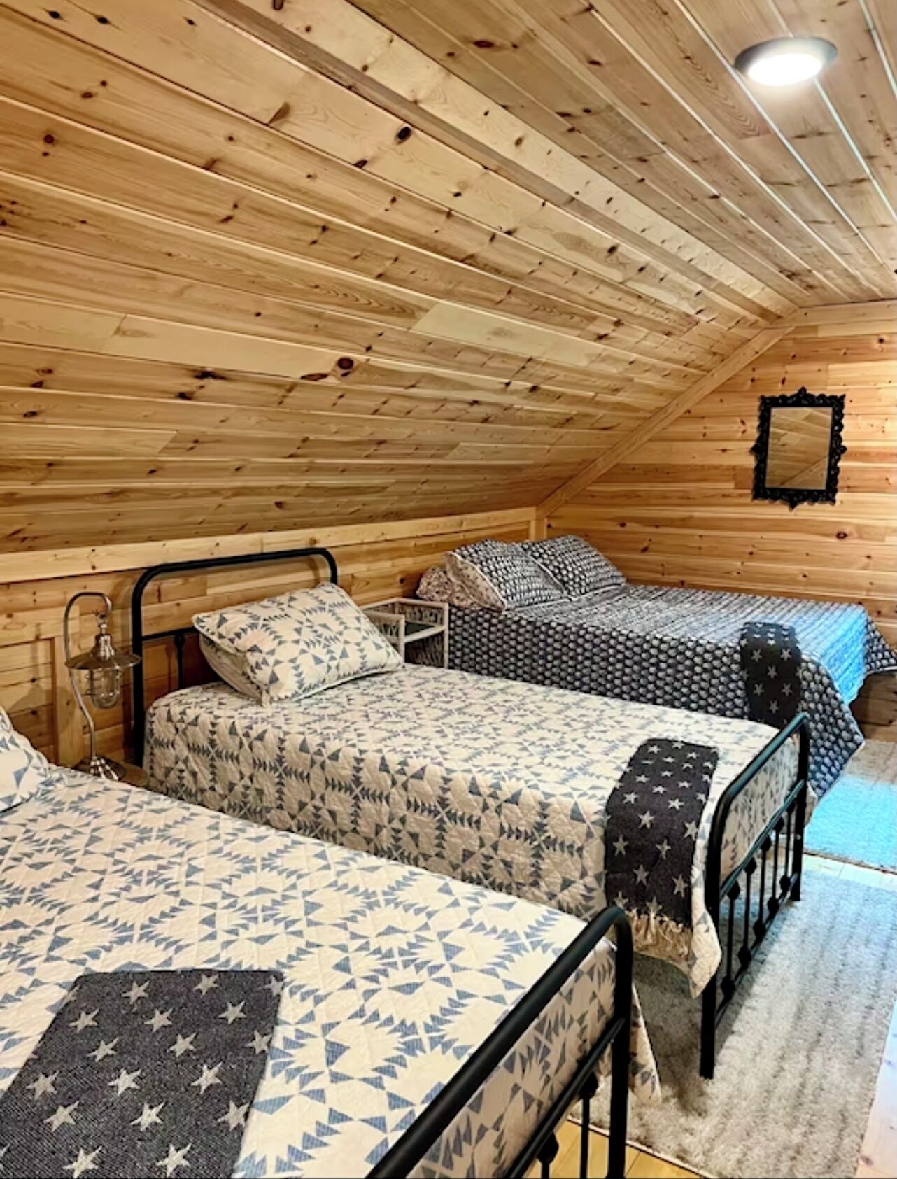 Une chambre confortable située dans les combles, avec des murs en bois et un plafond en pente, comprenant deux lits avec une literie à motifs et une petite table.