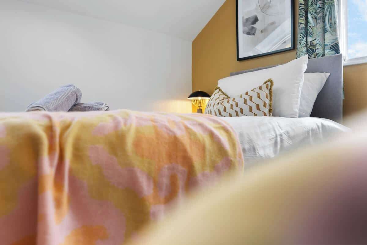 A hotel room with a bed, pillows, a lamp, and a framed picture on the wall.
