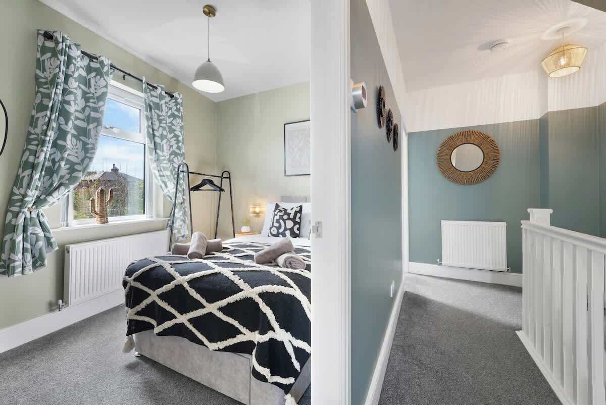 A bedroom with a bed, window, radiator, and a bathroom with a mirror and radiator.
